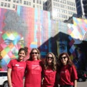 Four women with red shirts posing in front of Dylan mural