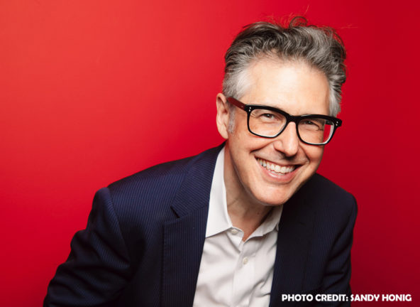 Ira Glass smiling with red background; Credit Sandy Honig