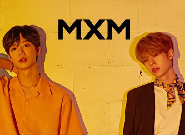 MXM, with two people standing against yellow block wall.