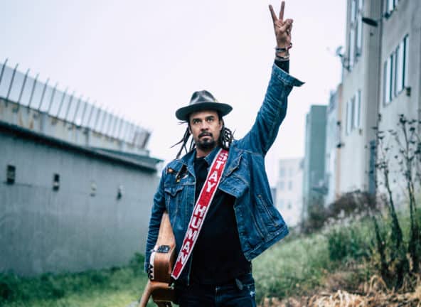 Michael Franti with guitar and holding up peace sign