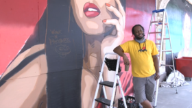 Visual artist Reggie LeFlore standing next to his mural of the Overseer