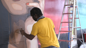 Visual artist Reggie LeFlore uses a spray paint can to work on his mural of the Overseer