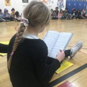 A girl reading a script while sitting on a gym floor