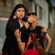 Chad Germann portrait of a Native woman wearing red, shielding her daughters eyes