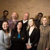 TC Pride Board members standing in a group, smiling and joking, in front of a pale brick wall.