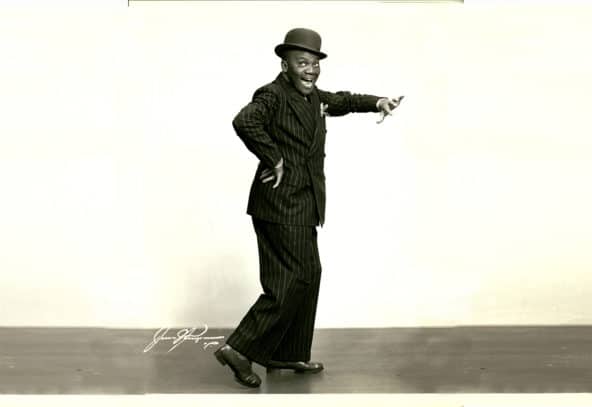 Man in stripped suit and bowler top hat taps a toe with left hand raised and right hand on hip. Photo Credit: Hennepin County Library