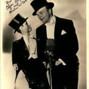 Man in tuxedo and top had stands next to and slightly behind a ventriloquist puppet with same outfit and monocle, both behind an NBC microphone. Photo Credit: Hennepin County Public Library