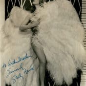 Woman stands flanked by huge costume wings and leg prominently placed forward while looking up to the right. Photo Credit: Hennepin County Public Library