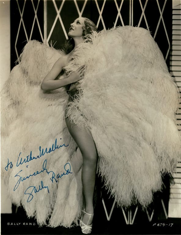 Woman stands flanked by huge costume wings and leg prominently placed forward while looking up to the right. Photo Credit: Hennepin County Public Library