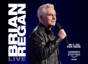 Brian Regan Live; Dec 31, 2023; State Theatre; Brian with white hair wearing a leather jacket and holding a microphone to his mouth;