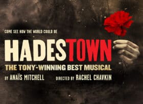 Hadestown grungy black background with a red carnation held in a hand