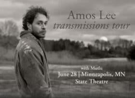 black and white photo of amos lee wearing a denim jacket with a rural background in the distance