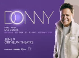 Donny Osmond smiling and wearing a white jacket and white tshirt